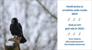 Kuvassa naakka seisoo talvisessa maisemassa puun päällä ja katsoo sivulle. Kuvassa on valkoinen alue, jossa on kuvituksena linnun jälkiä sekä joulun ja uuden vuoden toivotus suomeksi ja ruotsiksi.